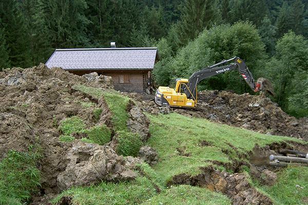 Neben Alphütte ein Bagger der baggert